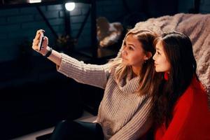 Dos chicas lindas con suéteres de punto se toman selfies en un teléfono inteligente