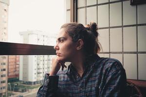 Worried woman looking from the window of her flat