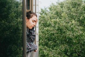 Mujer preocupada cerca de la ventana en la ciudad durante un día de primavera foto