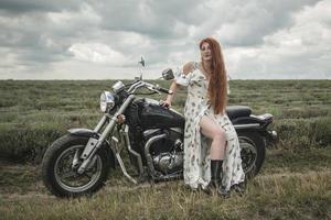 Chica pelirroja con un vestido blanco y botas junto con un campo de lavanda en motocicleta foto