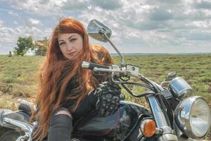 The red haired biker girl is sitting on a motorcycle field of meadow and clouds photo