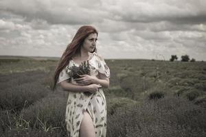 Retrato de una joven pelirroja con un vestido blanco en un campo con un ramo de lavanda foto