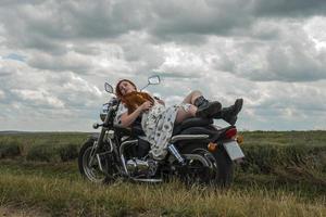 Chica pelirroja con un vestido blanco y botas junto con un campo de lavanda en motocicleta foto