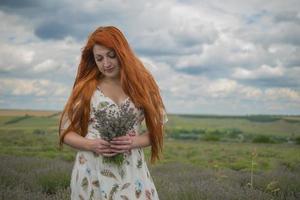 portrait of a red haired young girl in a white dress in a field with a bouquet of lavender photo