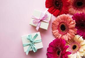 flores de gerbera y cajas de regalo sobre un fondo rosa foto