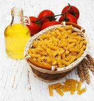 Cesta con pasta fusilli y tomate sobre una mesa de madera antigua foto