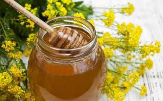 Jar of honey with rapeseed flowers on a wooden background photo