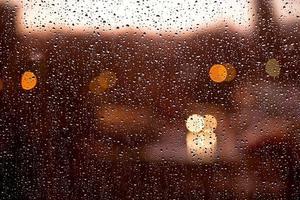 Water drops on window with sunset blurred lights after the rain