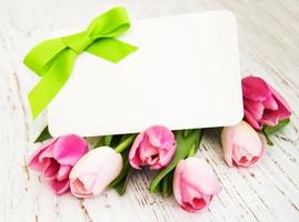 Tulipanes rosados y amarillos con una tarjeta sobre un fondo de madera blanca foto