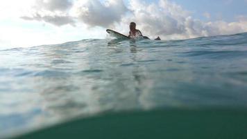 Surfer paddles in ocean and splashes camera video