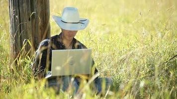 Cowboy sits in grass using laptop computer video