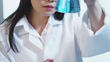 Woman in science lab looking at beaker of liquid. video