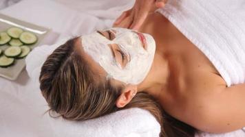 Woman at spa with facial mask and cucumbers video
