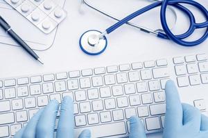 Doctor manos en guantes escribiendo en el teclado de la computadora, telemedicina o tecnología médica concepto de fondo vista superior foto