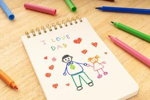 Fathers day concept Notebook with drawing of a father with a girl and marker pens on a wooden table photo