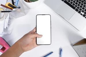 Man using a smartphone blank screen mock up at the white office desk photo