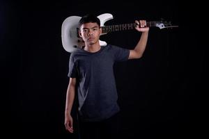 Young man in black leather jacket with electric guitar against black background in studio photo