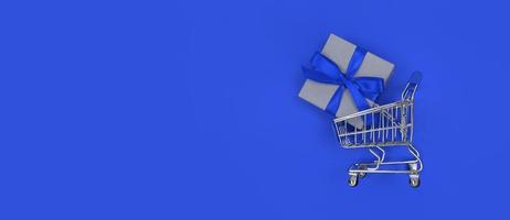 Supermarket trolley and gift box on blue background with copy space Shopping concept photo