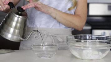 Woman pouring water in a glass bowl in kitchen with background
