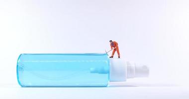 Figura de trabajador técnico de pie sobre una botella de spray de alcohol concepto covid19 foto