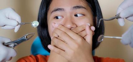 Chica asustada por dentistas cubre su boca en el consultorio del dentista