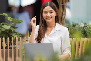 Joven mujer asiática sentada con cara sonriente con portátil en una ciudad foto