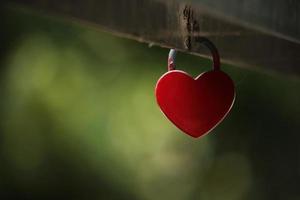 Small red heart padlock hanging on a bridge handrail photo