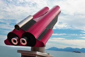 Red site seeing telescope pointing up on blue clouded sky and sea with yachts background photo