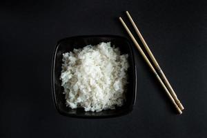 Bowl with boiled rice on black background photo