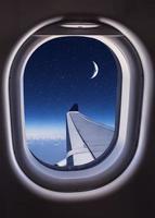 Aircraft window with the view of the wing and night sky