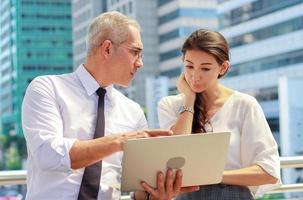 Business men and women stand and watch business and market information with their laptops in the outdoors in the modern downtown area photo