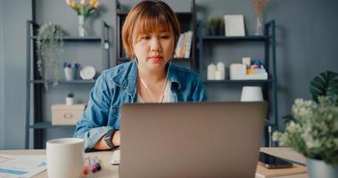 Asia businesswoman using laptop talk to colleagues about plan in video call while working from house at living room photo