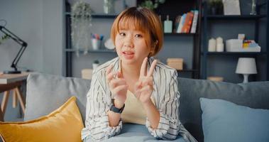 Asia businesswoman using laptop talk to colleagues about plan in video call while working from house at living room photo