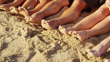 Group of young people with feet in sand, closeup video