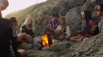 Gruppe junger Leute, die am Lagerfeuer am Strand rumhängen video