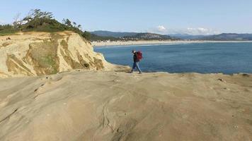 Aerial shot of backpacker walking on rock overlooking Pacific Ocean video