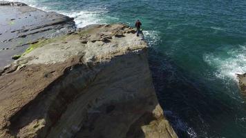 Aerial shot of backpacker standing on rock overlooking Pacific Ocean