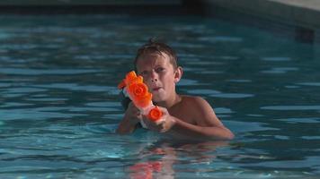 niño se zambulle en la piscina disparando pistola de agua, cámara super lenta video