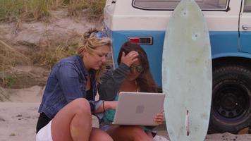 twee meisjes op het strand die naar een laptop kijken video