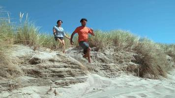 Couple at beach running down sand dune in super slow motion video