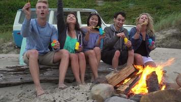 Group of friends at beach hanging out by campfire blowing bubbles
