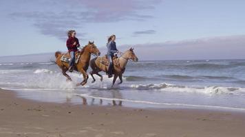 Women riding horses at beach in slow motion video