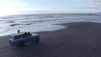 Aerial view of group of friends driving on beach in vintage vehicle