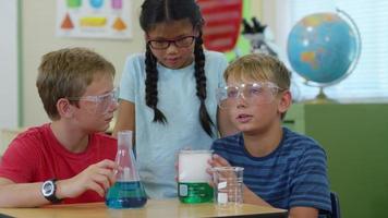 Three kids in classroom looking at science experiment video