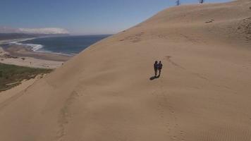 vista aerea della coppia che fa un'escursione sulle dune di sabbia alla spiaggia at video