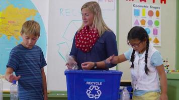 profesor y estudiantes en el aula de la escuela poniendo botellas en la papelera de reciclaje video