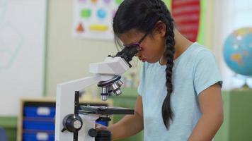 Young girl in school classroom looking into microscope video