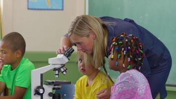 professor e alunos olham através de microscópios na sala de aula da escola