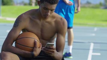 tonåring basketspelare använder mobiltelefon på utomhus domstol video