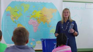 Teacher giving recycle lesson in school classroom and student goes up front to help video